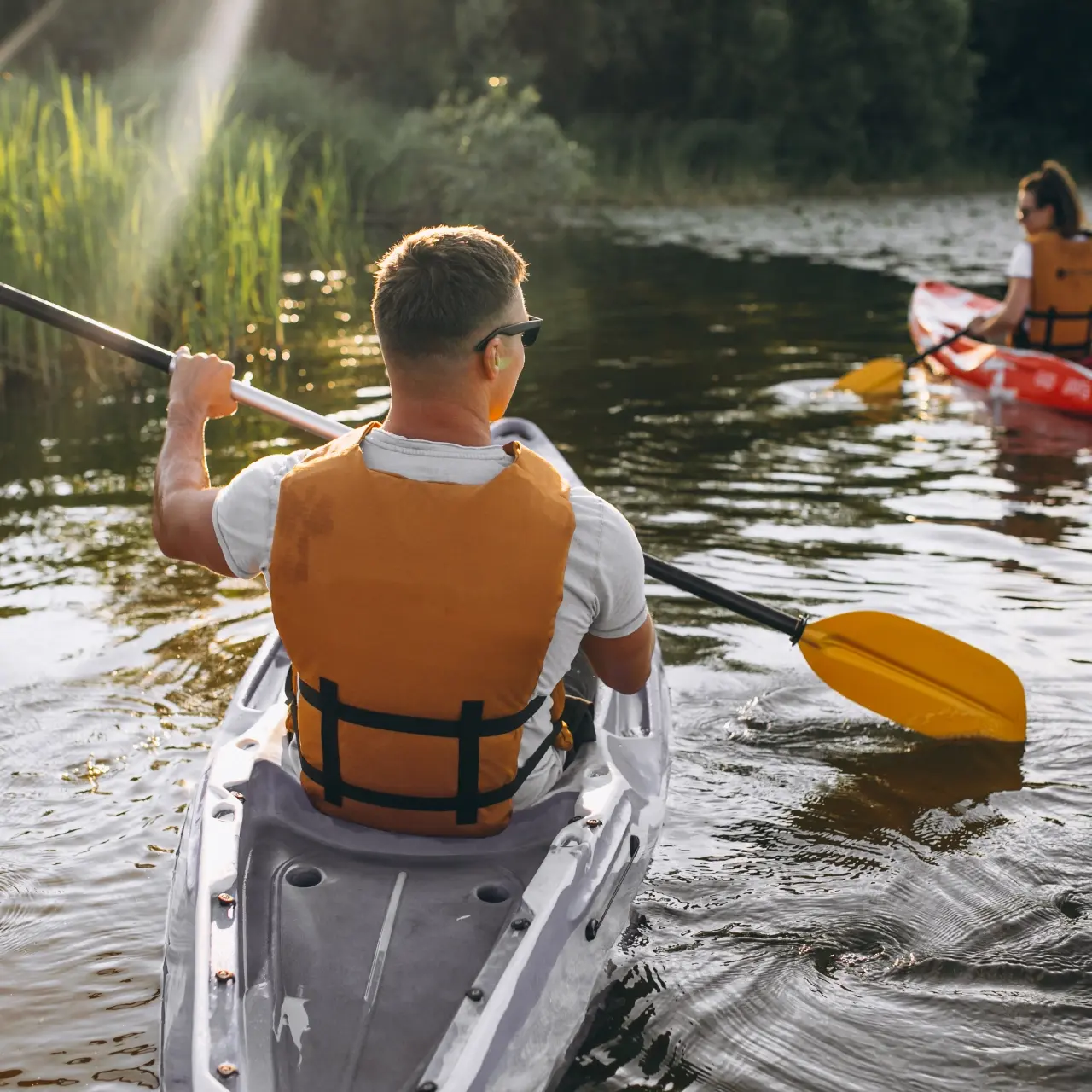 Two people kayaking along a calm, reed-lined river