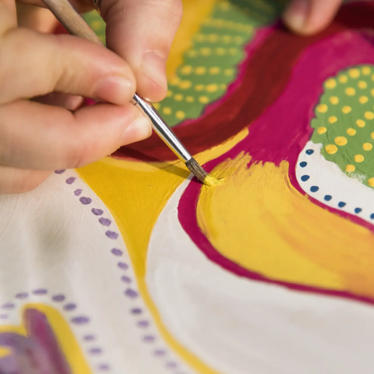 Hand painting yellow shapes on a colorful canvas at an art workshop