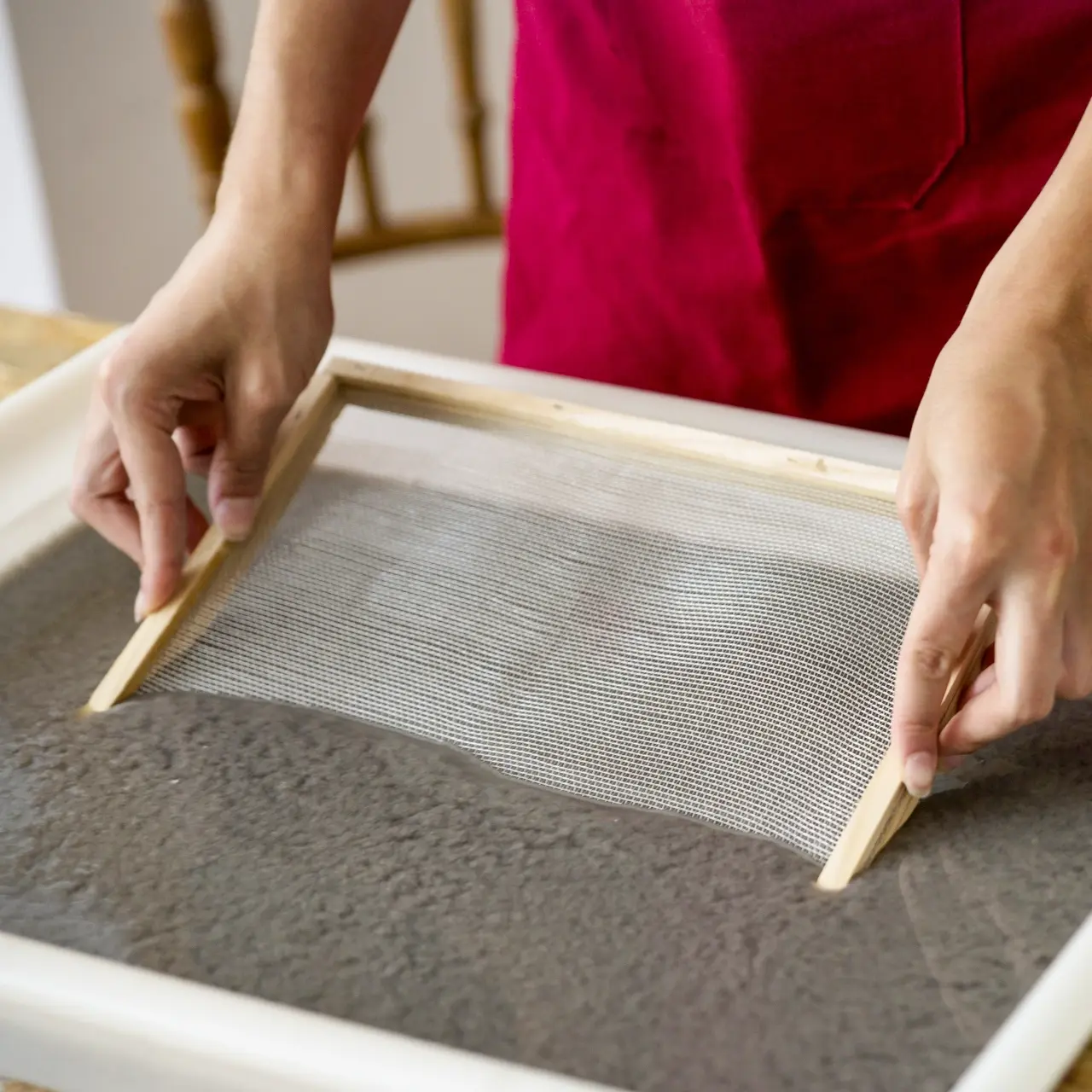 Hands lifting a mesh frame from paper pulp at a handmade paper workshop