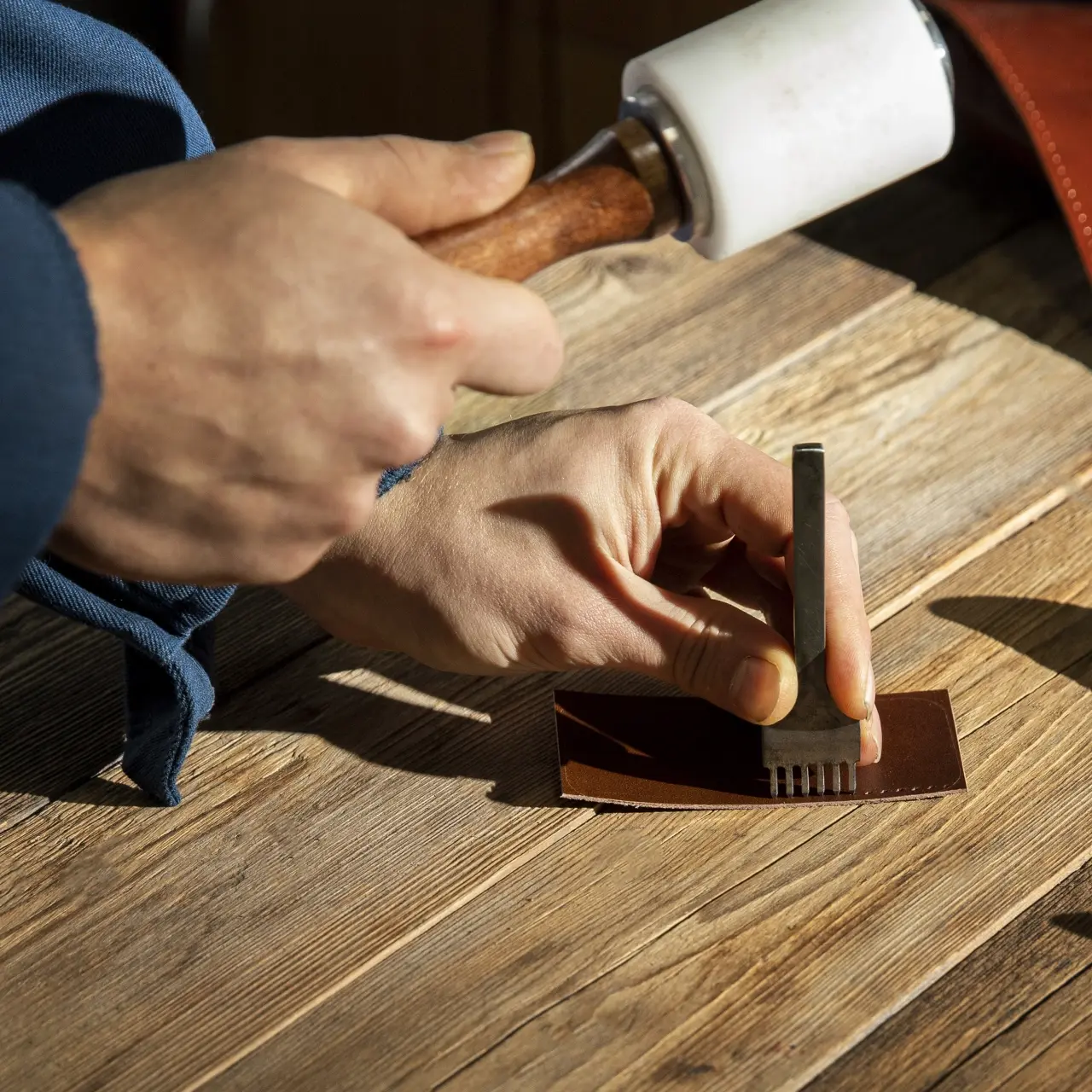 Hands using a stitching punch and mallet on leather at a craft workshop